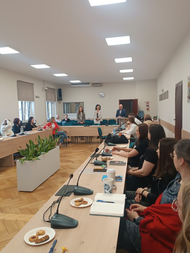 Zdjęcie z relacji wydarzenia. Przy stole w literę U siedzą ludzie i rozmawiają.