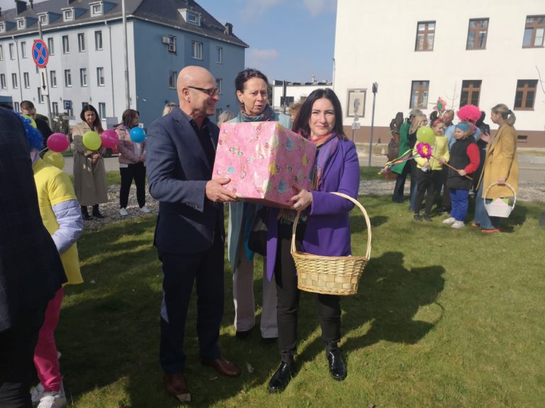 Zdjęcie z relacji wydarzenia. Trzy osoby trzymają prezent w rękach.